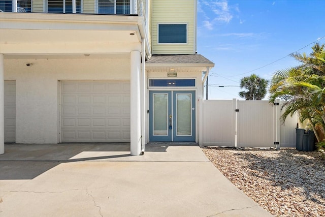 4717 Lemon Bay Dr, Venice, FL 34293 - view of exterior entry featuring fence, an attached garage, a shingled roof, concrete driveway, and french doors