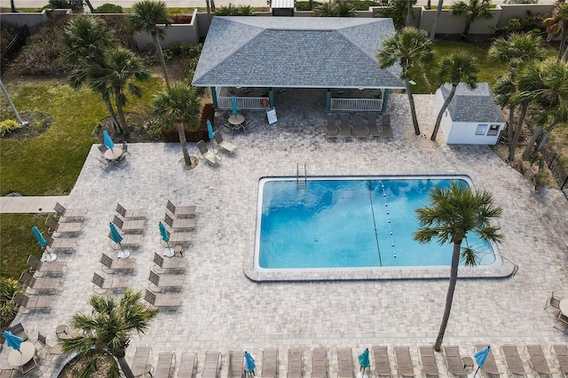 community pool with fence, an outdoor structure, and a patio area