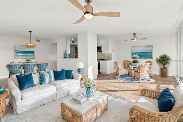 living room featuring baseboards, ceiling fan, light wood-style flooring, and visible vents