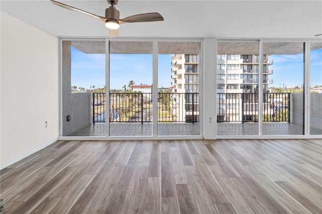 interior space with a ceiling fan, a wall of windows, a healthy amount of sunlight, and wood finished floors