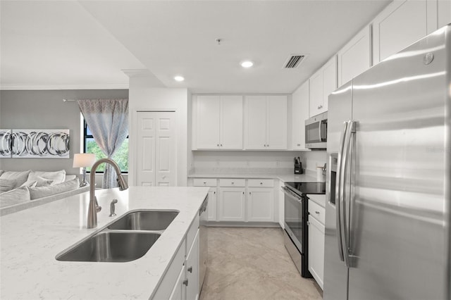 kitchen with appliances with stainless steel finishes, a sink, open floor plan, light stone countertops, and white cabinets