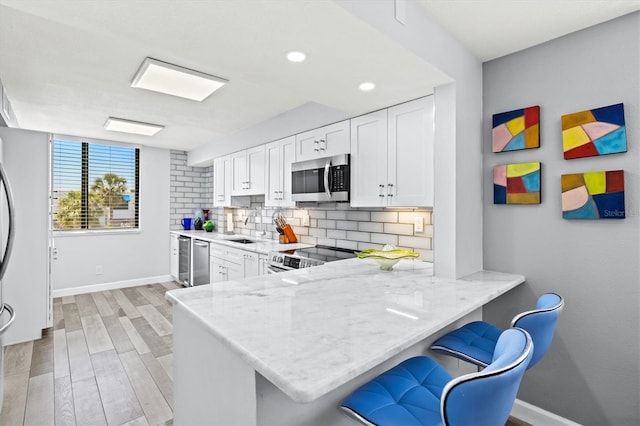 kitchen with baseboards, a sink, white cabinets, tasteful backsplash, and appliances with stainless steel finishes