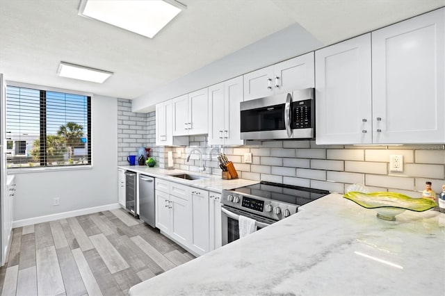 kitchen with backsplash, appliances with stainless steel finishes, white cabinetry, and a sink