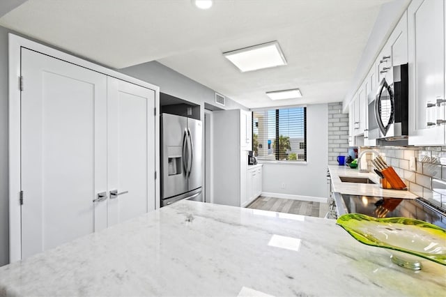 kitchen with a sink, light wood-type flooring, visible vents, light stone countertops, and appliances with stainless steel finishes