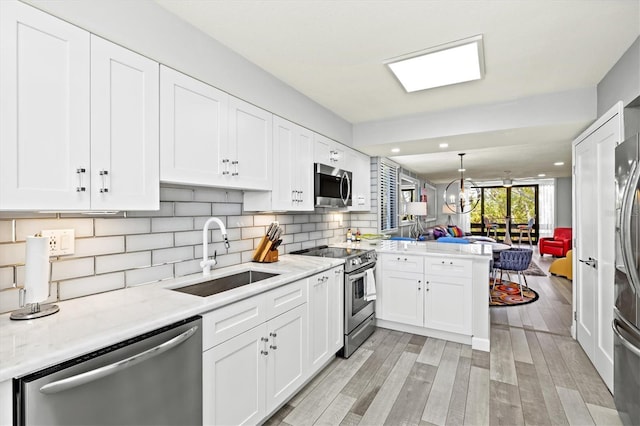 kitchen with a sink, a peninsula, stainless steel appliances, and white cabinets
