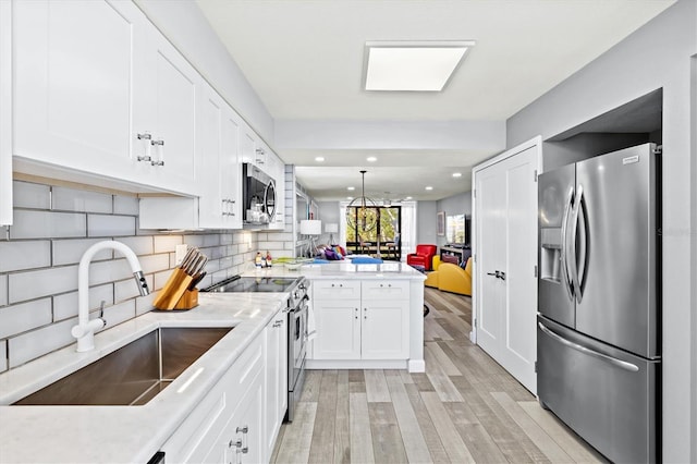 kitchen with a peninsula, light wood finished floors, a sink, stainless steel appliances, and white cabinets