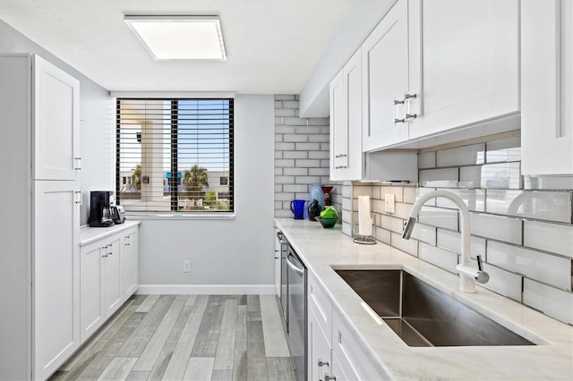 kitchen featuring light stone countertops, dishwasher, a sink, white cabinets, and tasteful backsplash