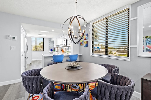 dining area with light wood-type flooring, a chandelier, baseboards, and a textured ceiling