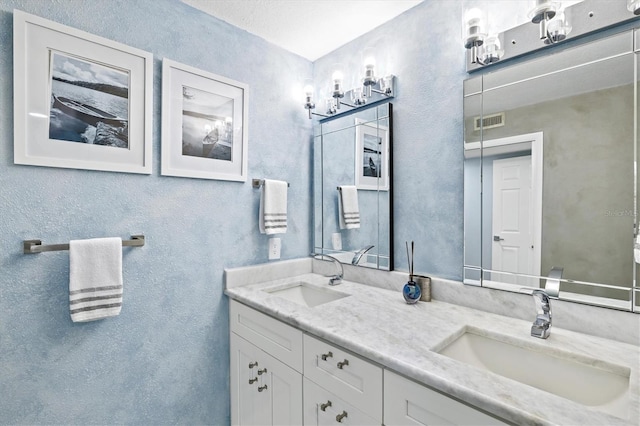bathroom with double vanity, a textured wall, visible vents, and a sink