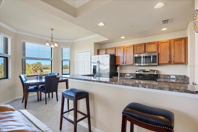 kitchen with stainless steel appliances, dark stone counters, a chandelier, crown molding, and a kitchen bar