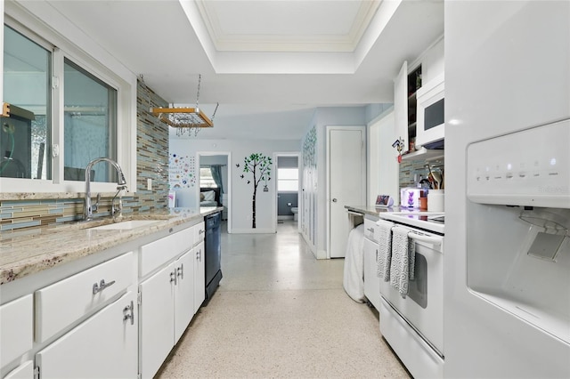 kitchen featuring a sink, a raised ceiling, white appliances, light speckled floor, and white cabinetry