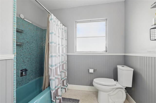 full bathroom featuring wainscoting, speckled floor, baseboards, toilet, and shower / tub combo with curtain