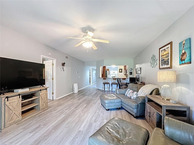 living room with light wood-style floors, visible vents, baseboards, and ceiling fan