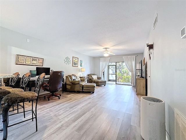 living area featuring a textured ceiling, a ceiling fan, visible vents, and light wood-style floors