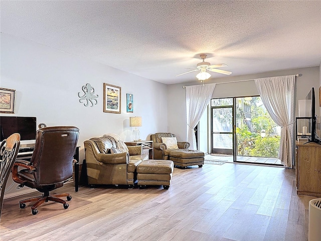 living area featuring light wood-style floors, a ceiling fan, and a textured ceiling