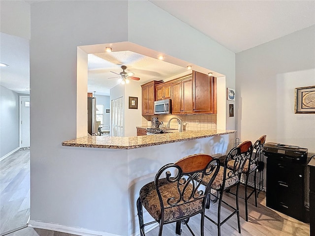 kitchen featuring light stone countertops, ceiling fan, brown cabinets, tasteful backsplash, and appliances with stainless steel finishes