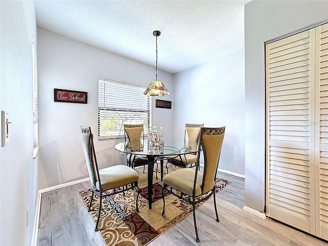 dining area featuring light wood-type flooring, baseboards, and a textured ceiling