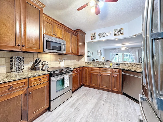 kitchen with a ceiling fan, brown cabinets, stainless steel appliances, and light wood-style flooring