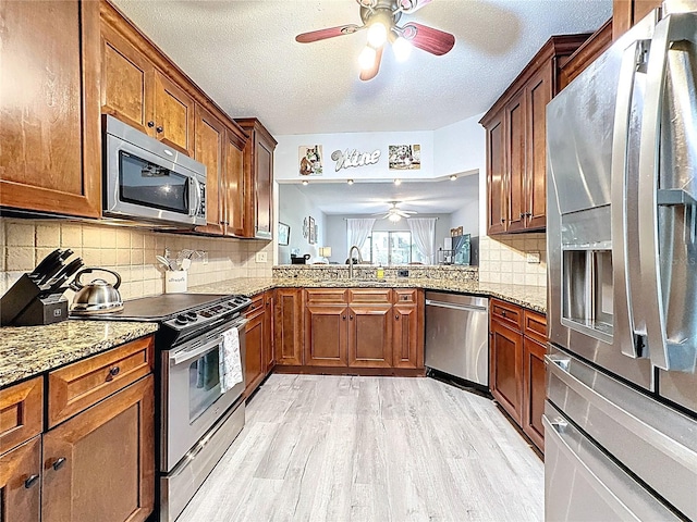 kitchen with light wood finished floors, a sink, light stone countertops, ceiling fan, and appliances with stainless steel finishes