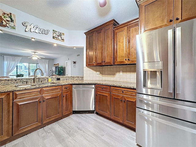 kitchen with light wood finished floors, brown cabinets, a sink, stainless steel appliances, and light stone countertops