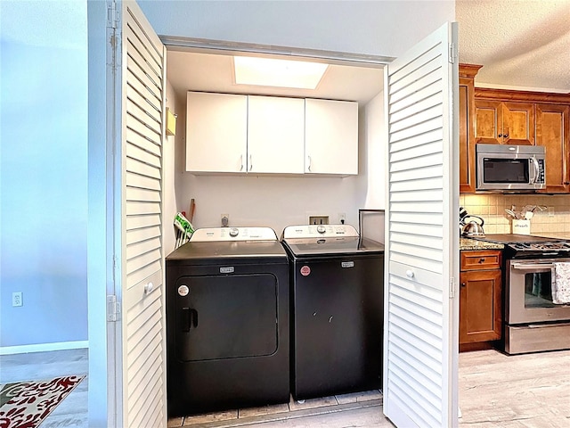 laundry room with a textured ceiling, light wood finished floors, cabinet space, and washer and clothes dryer