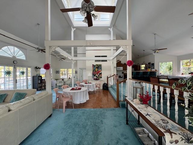 living room with carpet flooring, a skylight, ceiling fan, and high vaulted ceiling
