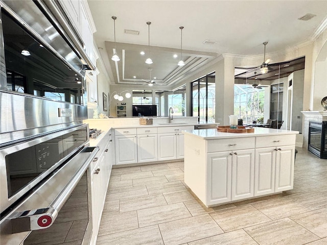 6919 Dominion Ln, Lakewood Ranch, FL 34202 - kitchen featuring a ceiling fan, ornamental molding, a kitchen island, a raised ceiling, and a glass covered fireplace