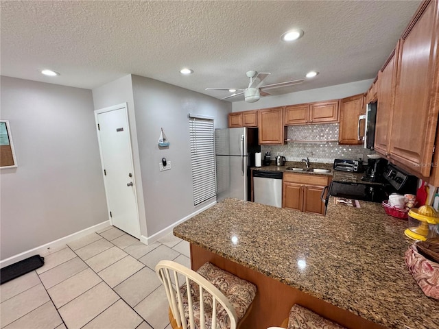 kitchen with ceiling fan, appliances with stainless steel finishes, a sink, baseboards, and a peninsula