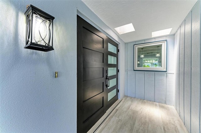 hallway with a skylight, a textured wall, and light wood-type flooring
