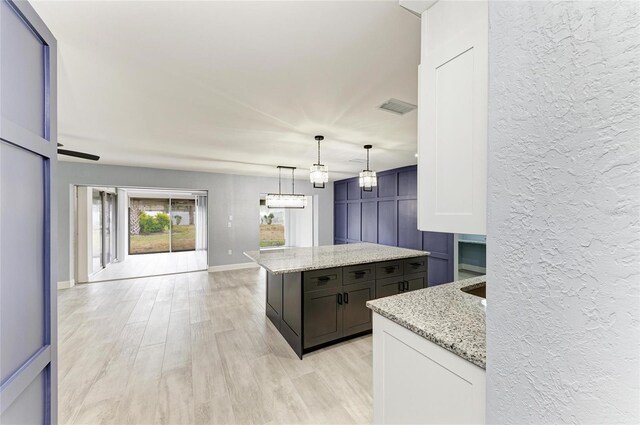 kitchen with visible vents, a center island, hanging light fixtures, light stone counters, and light wood finished floors
