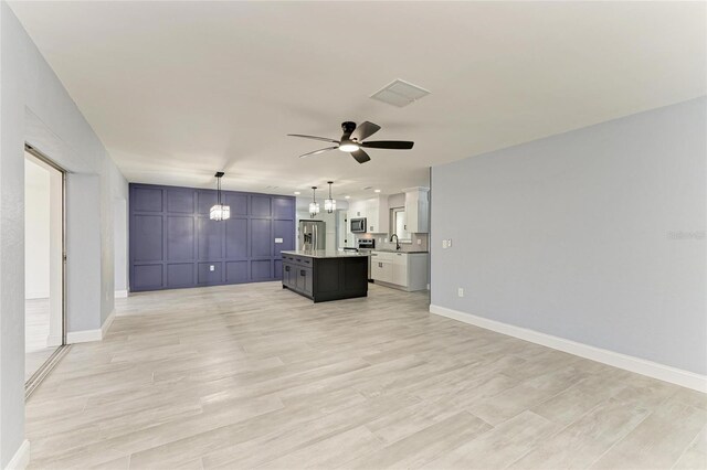 unfurnished living room featuring visible vents, light wood-type flooring, a sink, baseboards, and ceiling fan with notable chandelier