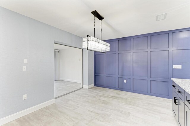 unfurnished dining area with visible vents, baseboards, a chandelier, a decorative wall, and light wood-style flooring