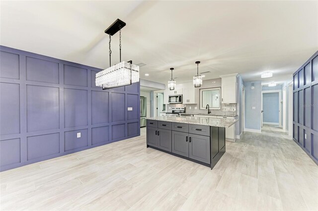 kitchen with appliances with stainless steel finishes, a center island, a sink, a decorative wall, and white cabinetry