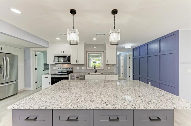 kitchen featuring appliances with stainless steel finishes, gray cabinets, light stone counters, and a notable chandelier