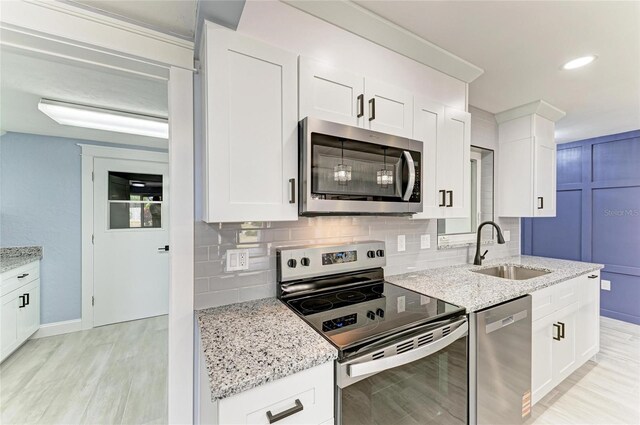 kitchen featuring tasteful backsplash, a sink, light stone counters, stainless steel appliances, and light wood-style flooring