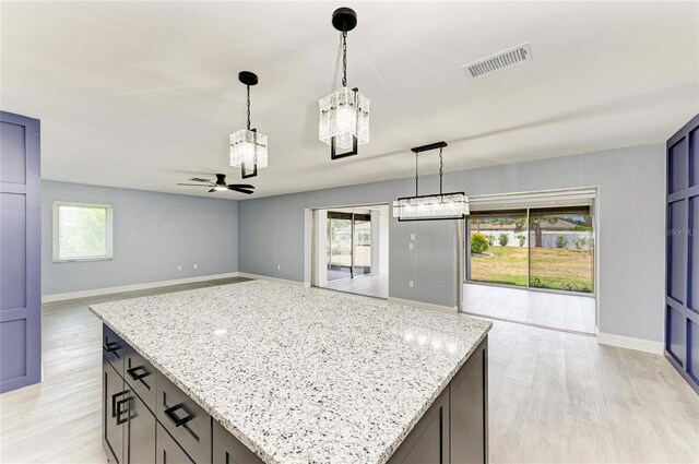 kitchen with a healthy amount of sunlight, light stone counters, ceiling fan with notable chandelier, and visible vents