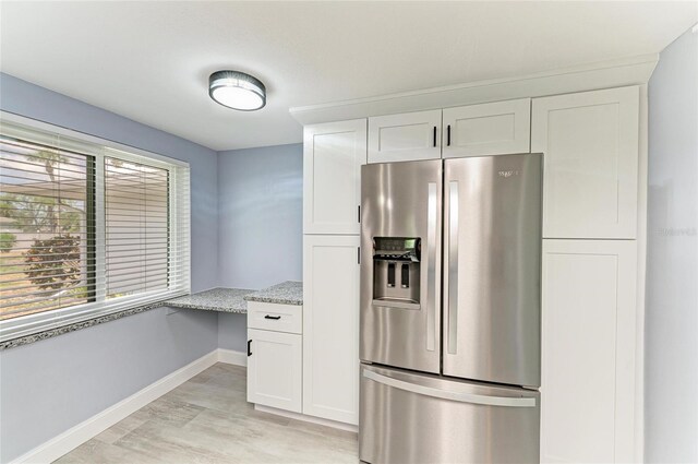 kitchen featuring stainless steel refrigerator with ice dispenser, light wood finished floors, baseboards, and white cabinetry