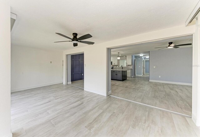 unfurnished living room with baseboards, a ceiling fan, light wood finished floors, and a sink