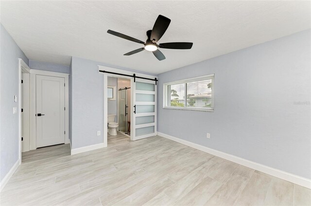 unfurnished bedroom featuring baseboards, a barn door, light wood finished floors, and ensuite bath