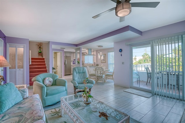 living room featuring a ceiling fan, baseboards, and stairway