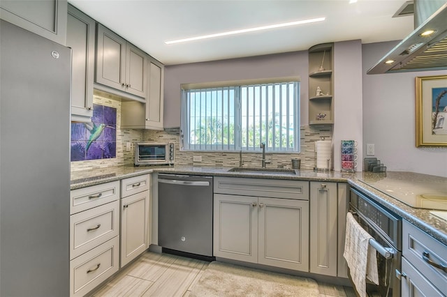 kitchen with exhaust hood, a sink, stainless steel appliances, backsplash, and gray cabinetry