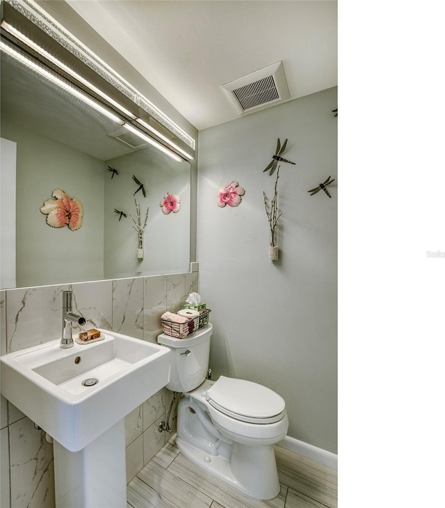 half bathroom with visible vents, a sink, toilet, and tile walls