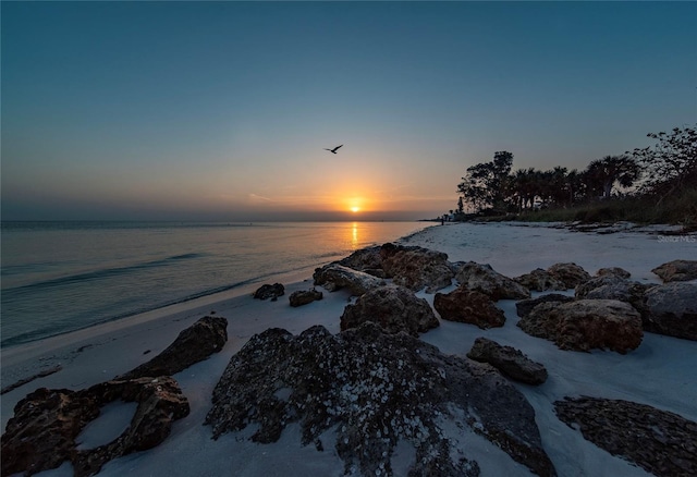 aerial view at dusk featuring a beach view and a water view