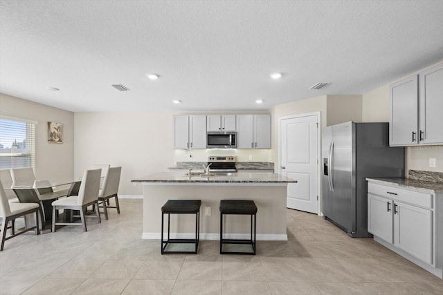 6314 Distant Haze Pl, Palmetto, FL 34221 - kitchen featuring appliances with stainless steel finishes, stone counters, a kitchen island with sink, a kitchen bar, and recessed lighting
