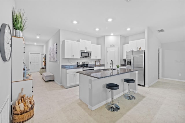 kitchen featuring a kitchen island with sink, a kitchen breakfast bar, dark stone countertops, stainless steel appliances, and light tile patterned floors