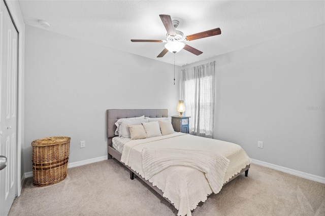 bedroom with baseboards, ceiling fan, a closet, and light colored carpet