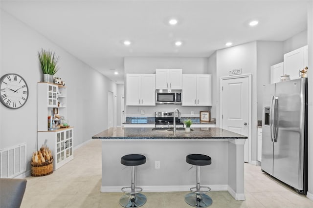 kitchen featuring visible vents, white cabinets, a sink, dark stone countertops, and appliances with stainless steel finishes