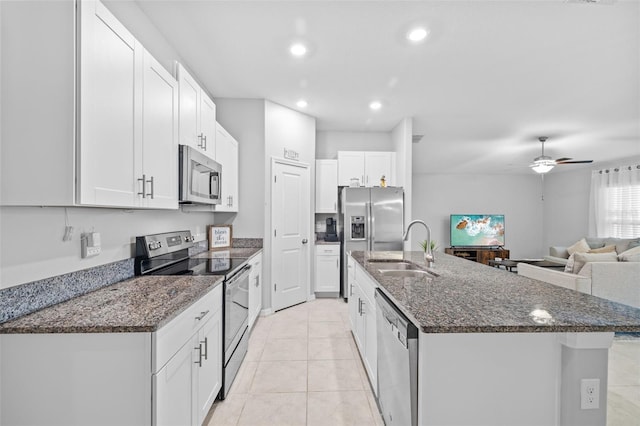 kitchen with appliances with stainless steel finishes, a sink, dark stone counters, white cabinetry, and a center island with sink