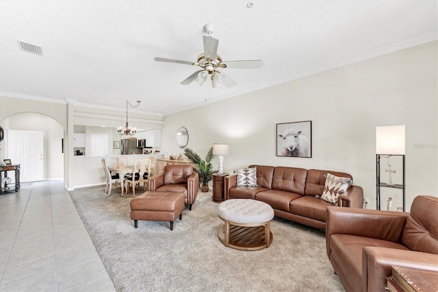 carpeted living area with crown molding, arched walkways, tile patterned floors, ceiling fan with notable chandelier, and visible vents