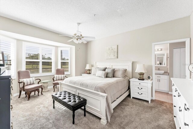 bedroom featuring a textured ceiling, connected bathroom, a ceiling fan, and light carpet
